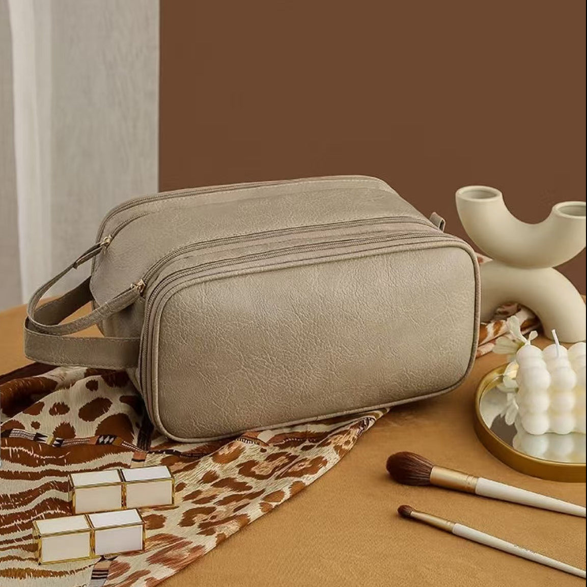 Beige toiletry bag on a table with makeup items and a bottle of perfume.