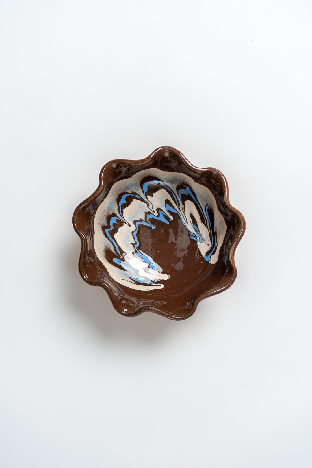 A small ceramic bowl with a marbled design and frill edge, predominantly in a brown color, against a white background. MIMMO Studios x Casa De Folklore